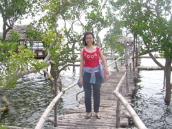 A visitor poses in a man-made bamboo bridge. Behind her are cottages made of native materials