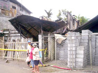 Passers-by look at the remains of the house that was turned into ashes, including six persons trapped in it, by a raging fire early morning yesterday.